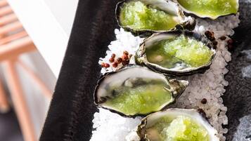 A tray of oysters on ice with a green topping, possibly a sauce or garnish, and some red peppercorns.
