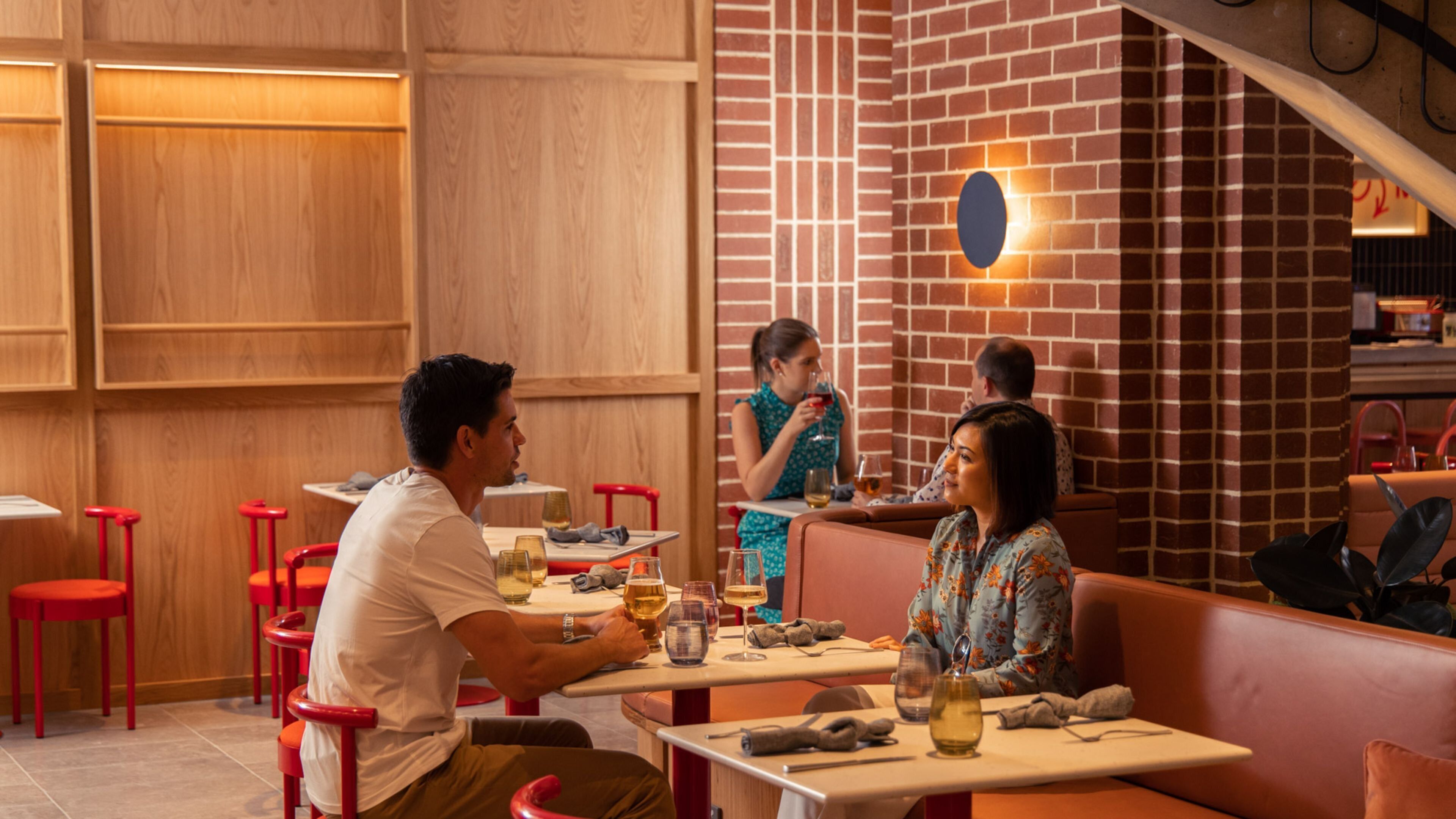 A restaurant interior with wooden panel walls, red bar stools, and a brick wall with a circular light fixture.
