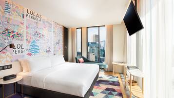 A hotel room with a large bed, a desk, a chair, a TV, and a window with a city view.