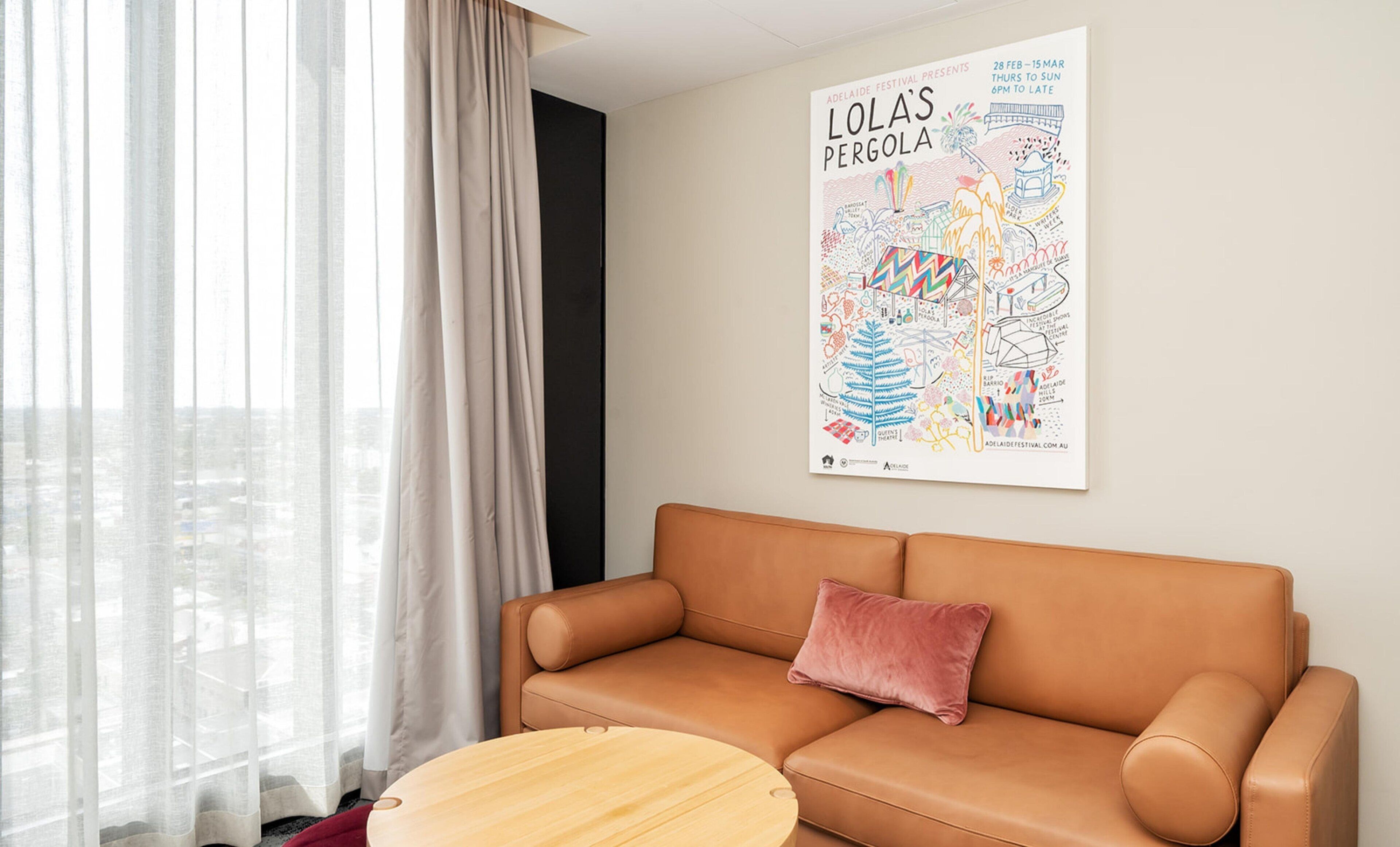 Ein modernes Wohnzimmer mit einer sandfarbenen Ledersofa, einem runden Holztisch und einem farbenfrohen Poster über Sehenswürdigkeiten in Adelaide.