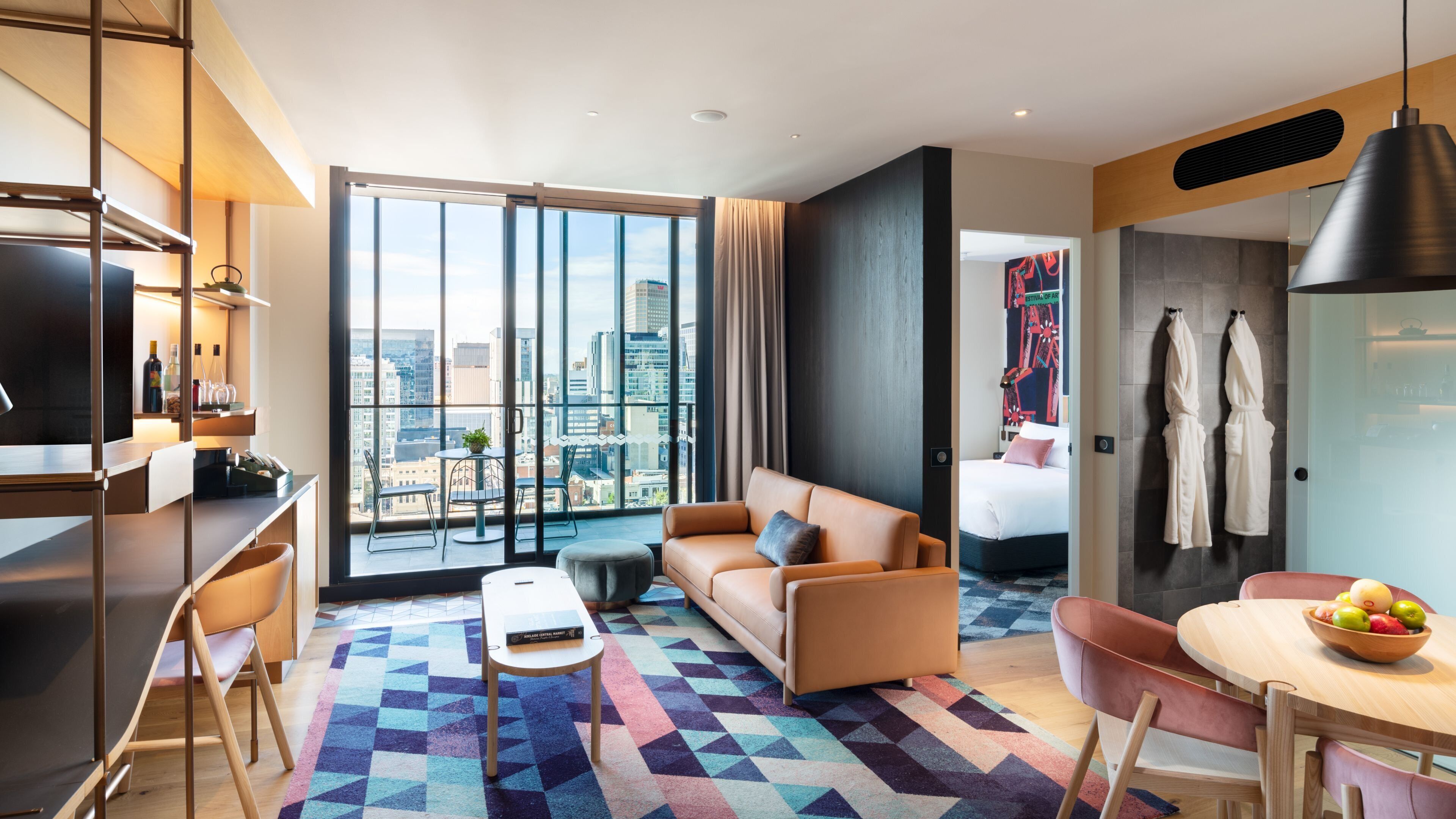 Una habitación de hotel moderna con un ventanal grande, un sofá, una mesa de comedor y una cama.