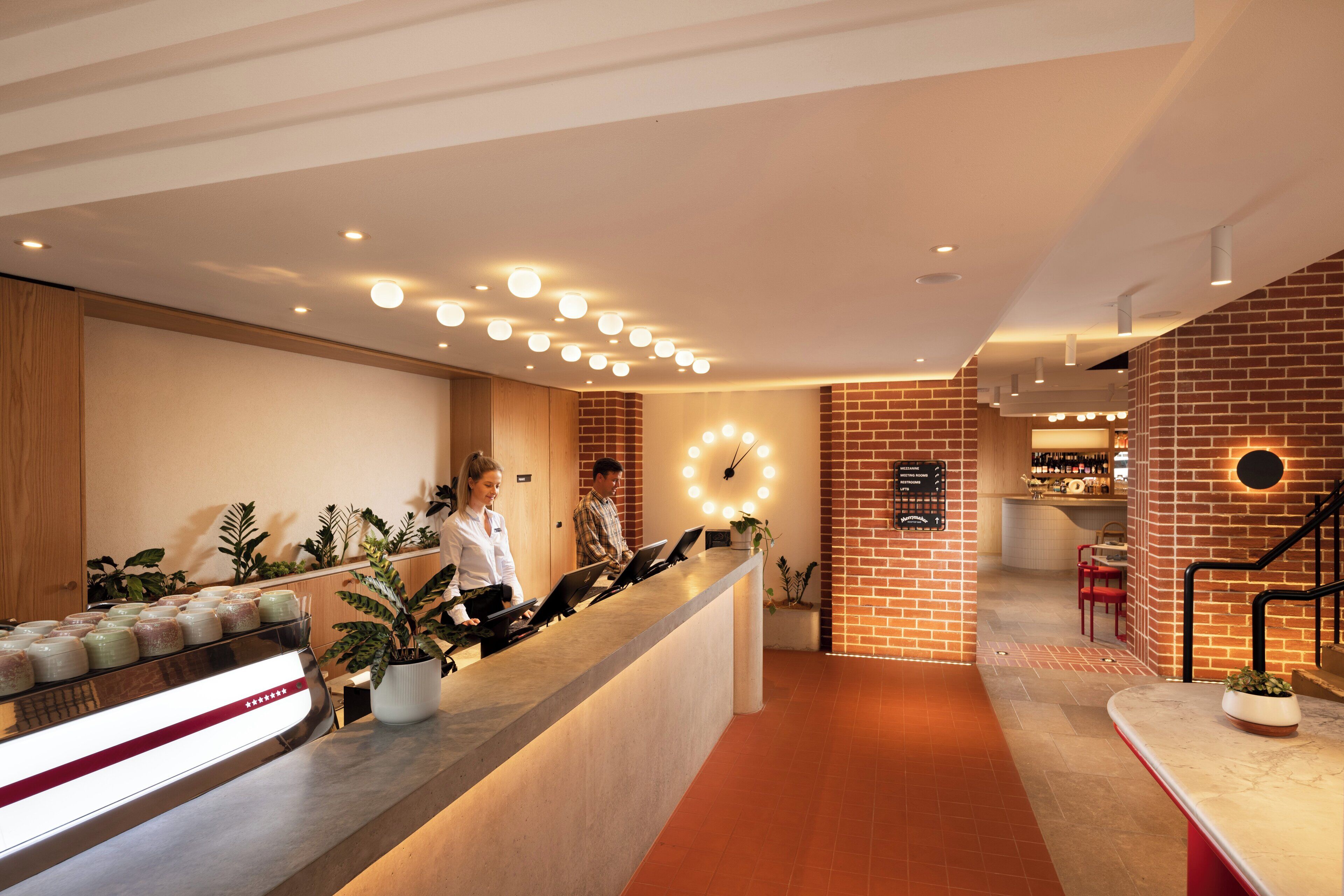 A reception area with a counter, potted plants, a clock, and a staircase.