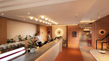 A reception area with a counter, potted plants, a clock, and a staircase.
