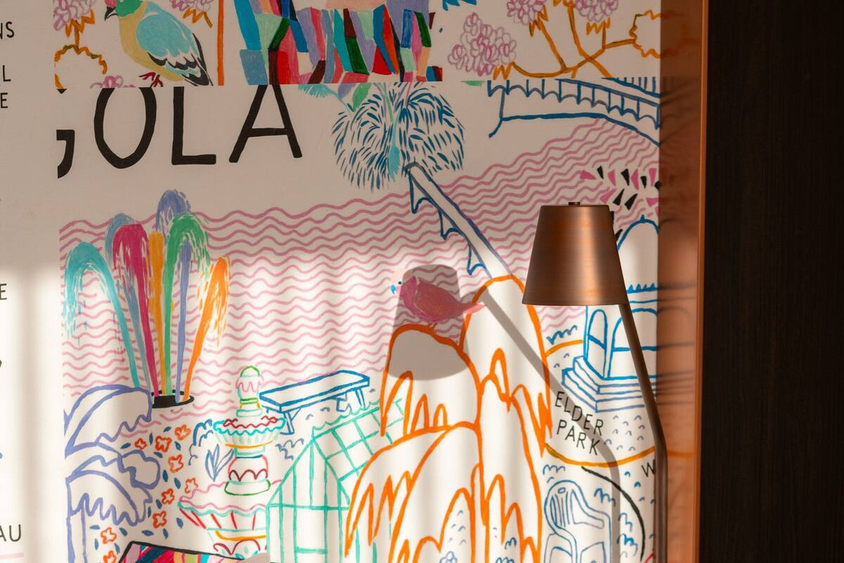 A hotel room with a bed, a bedside table with a lamp, and a wall with colorful artwork.