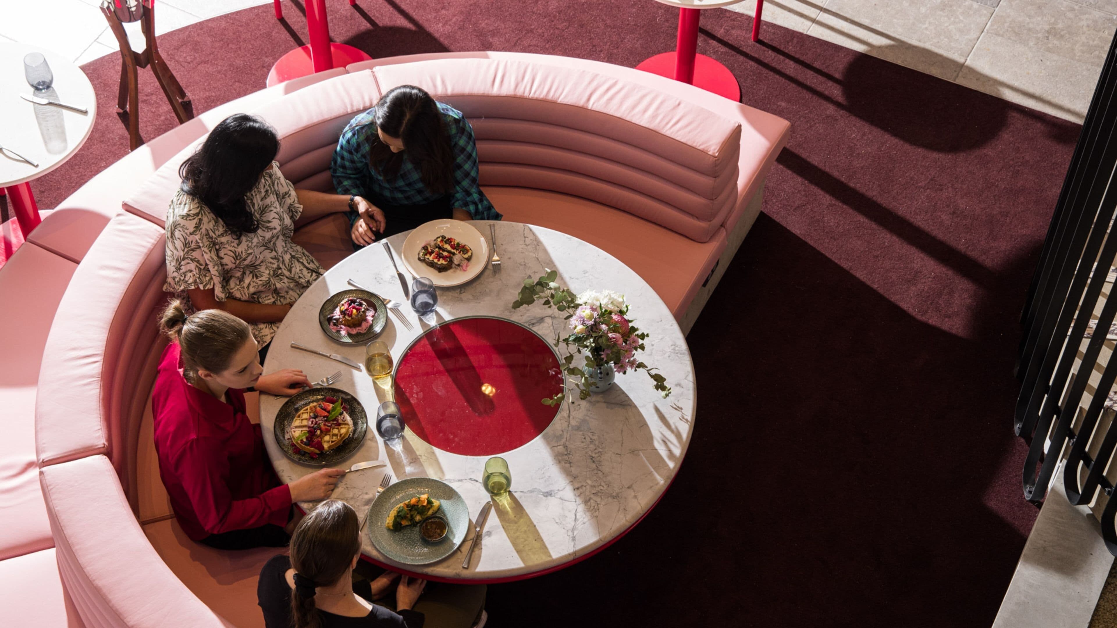 A round table with a red centerpiece surrounded by four people seated.