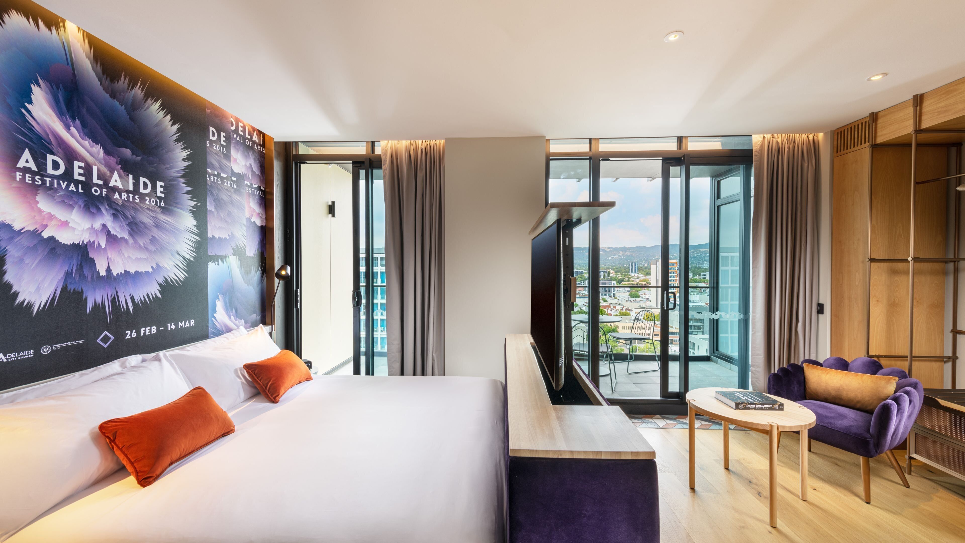 A hotel room with a bed, a TV, a balcony with a view, and a poster on the wall.
