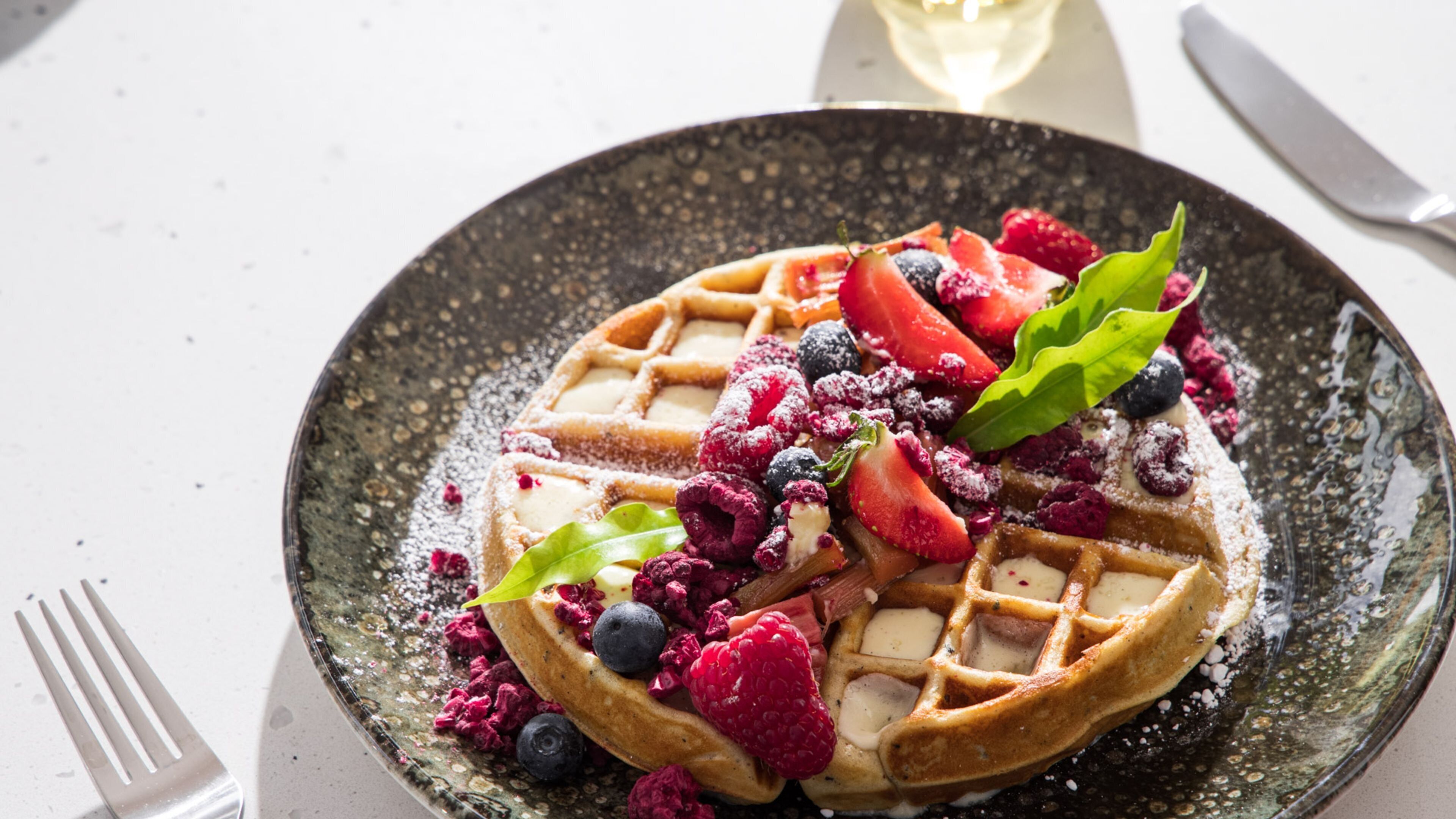 A plate with a waffle, berries, and a green leaf garnish.