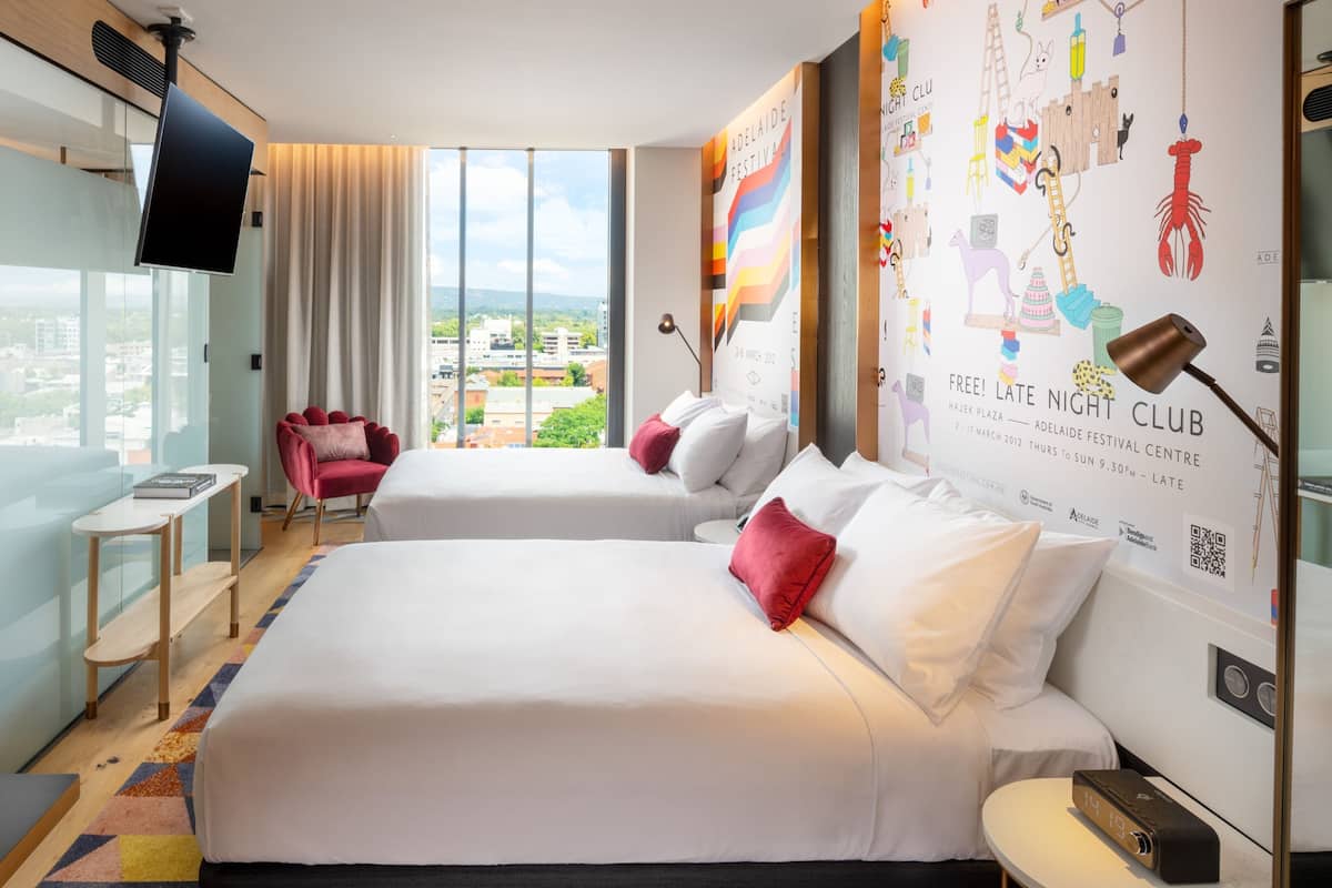A modern hotel room with a large bed, a small desk, a chair, and a TV.