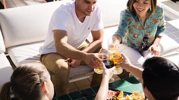 A group of people seated on a white outdoor sofa, holding glasses of beverages, with a table in front of them.