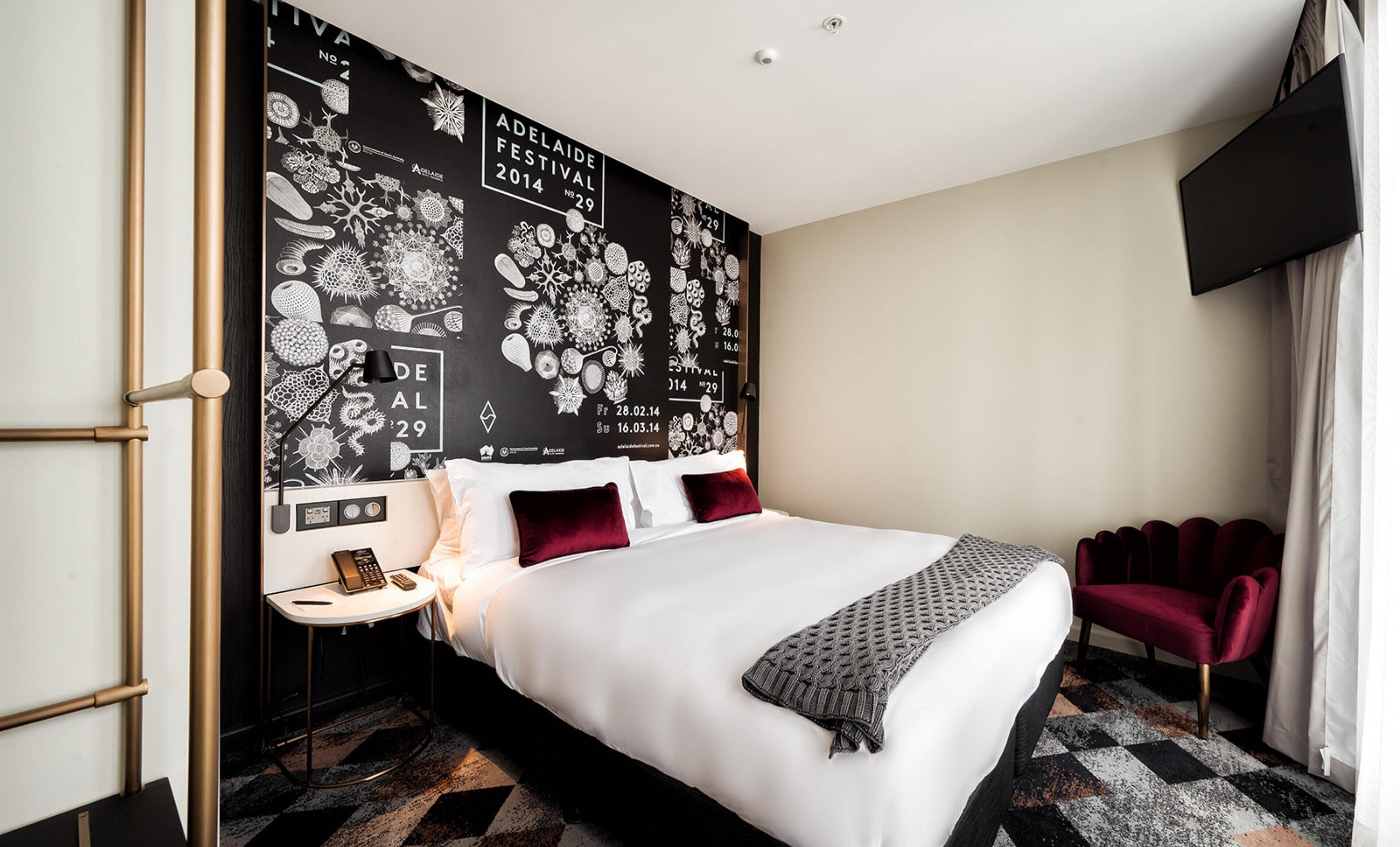 Una camera d'albergo moderna con un letto grande, un comodino con una lampada, una TV a parete e una moquette fantasia.