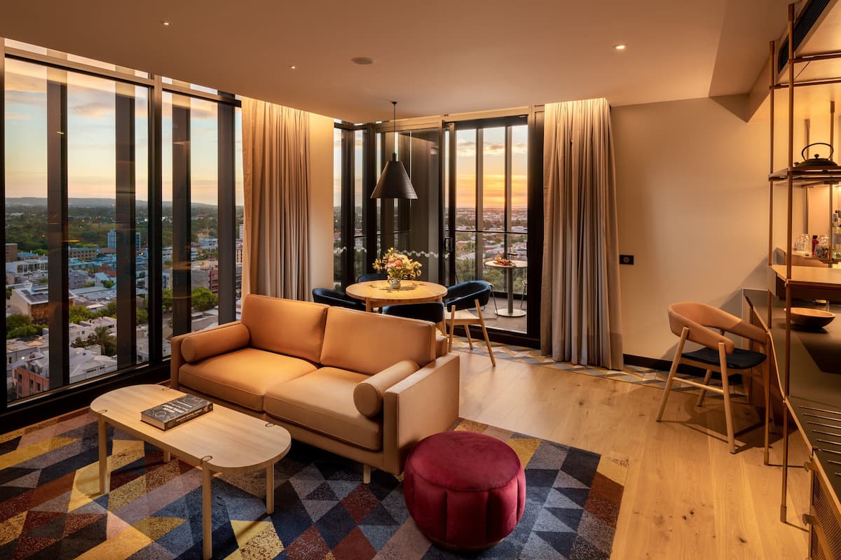 A modern living room with a sofa, coffee table, and ottoman, a dining area with a table and chairs, and large windows offering a city view.
