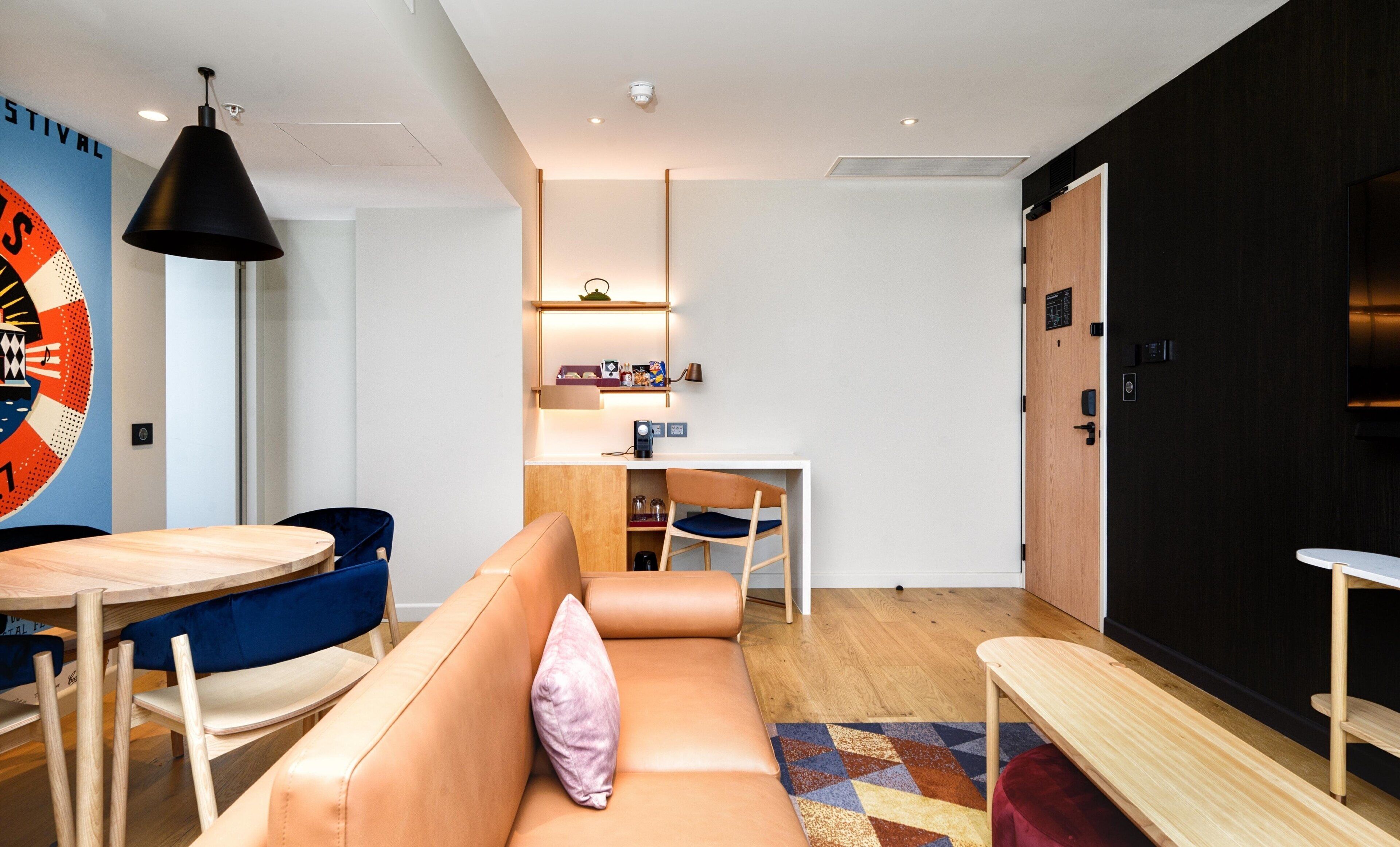 Une pièce moderne et bien éclairée, dotée d’un plancher en bois, d’un canapé avec un coussin, d’une petite table, d’un bureau avec des étagères et d’une étagère murale où sont disposés divers objets.