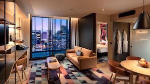 Quarto de hotel moderno com vista para a cidade, um sofá, uma mesa de jantar e uma área de quarto separada.