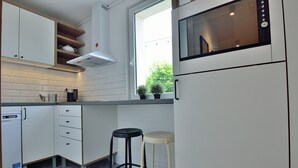 Kompakti keittiö, jossa on valkoiset kaapit, mikroaaltouuni, ikkunalaudalla kasveja ja kuviollinen lattia.