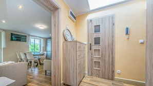 A modern kitchen with wooden cabinets, a dining area with white chairs, and a large window providing natural light. - Victus Apartamenty - Meru (Sopot)