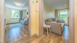 A modern living room with a sofa, a chair, and a view of the outdoors through a window. - Victus Apartamenty - Meru (Sopot)