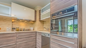 A modern kitchen with built-in appliances, wooden cabinetry, and a view of greenery outside. - Victus Apartamenty - Meru (Sopot)