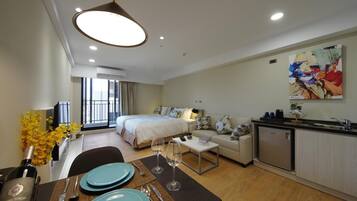 Una habitación de hotel moderna con una cama, un sofá, un comedor con una mesa para dos personas y una kitchenette.