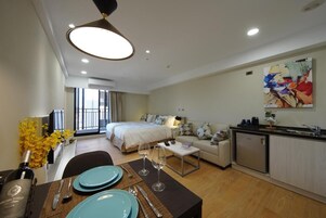 Una habitación de hotel moderna con una cama, un sofá, un comedor con una mesa para dos personas y una kitchenette.