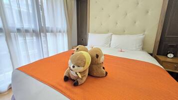 A hotel room with a large bed, a tufted headboard, and two plush toys on the bed.