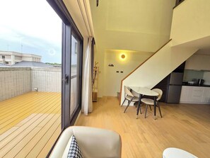 Um apartamento moderno com varanda de madeira, área de jantar com mesa e cadeiras, cozinha e escada.