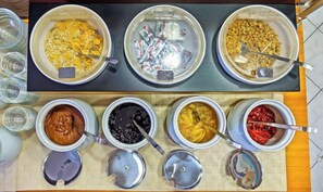 A buffet with various food items in bowls and containers, including oatmeal, cereal, and different sauces. - Nereides Hotel Apartments (Alonissos)