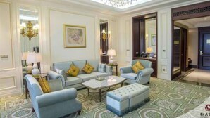 Quarto de hotel luxuoso com design clássico, apresentando um amplo sofá, uma mesa de centro e um tapete estampado.
