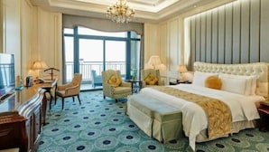 Quarto de hotel com uma cama grande, duas poltronas, uma escrivaninha e um lustre.