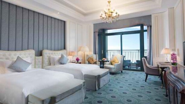 Quarto de hotel com duas camas, um candelabro, uma varanda com vista e um tapete estampado.