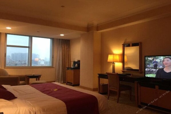 A hotel room with a bed, a desk, a television, and a window with a city view.