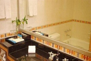 Un baño con un espejo grande, una bañera y un lavabo con artículos de aseo.