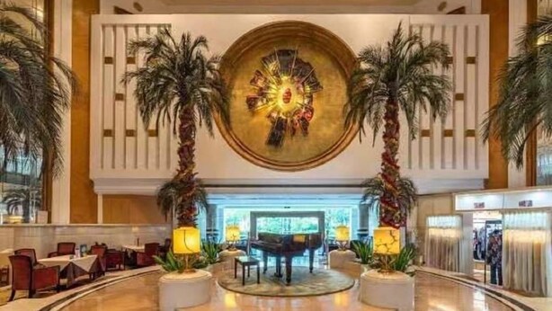 A lobby with a central circular artwork, palm trees, and a piano. - Panyu Guest House (Guangzhou)