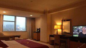 A hotel room with a bed, a desk, a television, and a view of the city through large windows. - Panyu Guest House (Guangzhou)