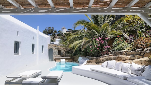 A white villa with a pool, outdoor seating, and a view of a windmill and lush greenery. - Great location over Mykonos Town, 294sqm 5 Bedrooms amazing sunset & sea views  (Mikonos)