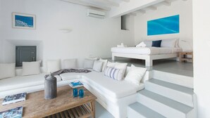 A modern, white-themed bedroom with a bed, a sofa, and a small table with books and a lamp. - Great location over Mykonos Town, 294sqm 5 Bedrooms amazing sunset & sea views  (Mikonos)