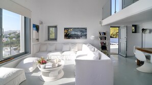 A modern living room with a white sectional sofa, a coffee table with flowers, and a bookshelf. - Great location over Mykonos Town, 294sqm 5 Bedrooms amazing sunset & sea views  (Mikonos)