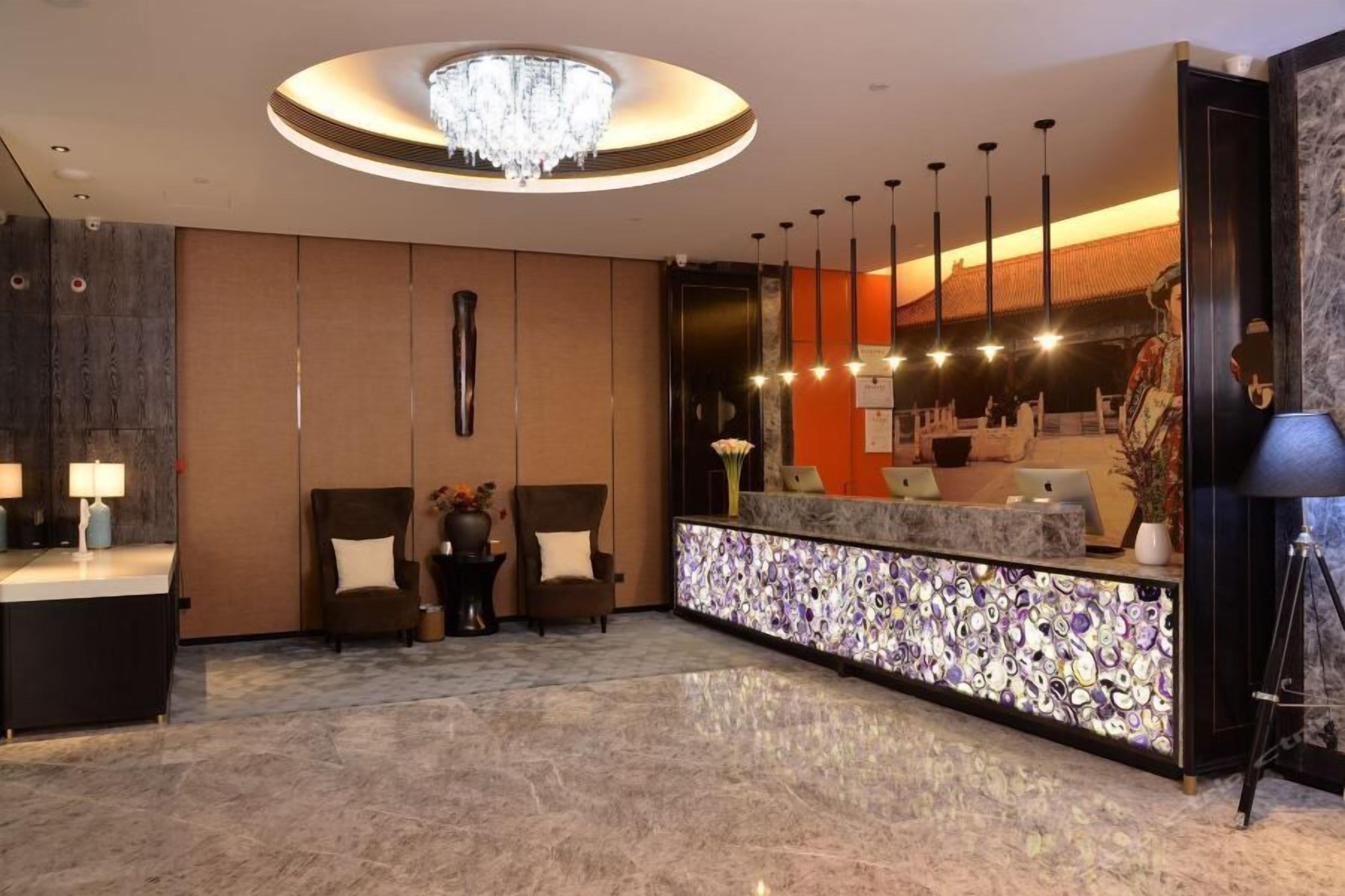 A modern lobby with a reception desk, two armchairs, a chandelier, and a decorative wall.