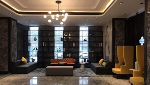 A modern lobby with a marble floor, a central seating area with a sofa and ottoman, a bookshelf, and two yellow armchairs. - Paco Hotel (Shenzhen)