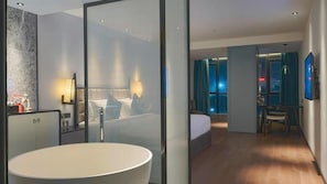A modern hotel room with a large bathtub, a bed with a view of the city, a dining area, and a separate bathroom. - Paco Hotel (Shenzhen)