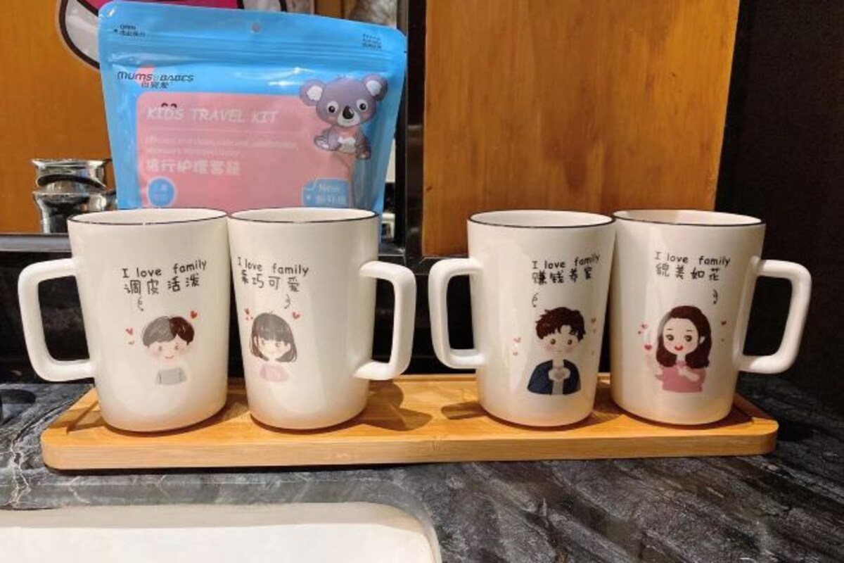 Four white mugs with illustrations and text on a wooden tray.