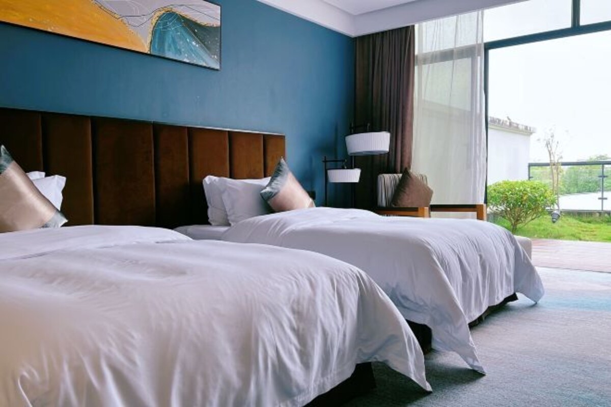 A hotel room with two beds, a large window, and a painting on the wall.