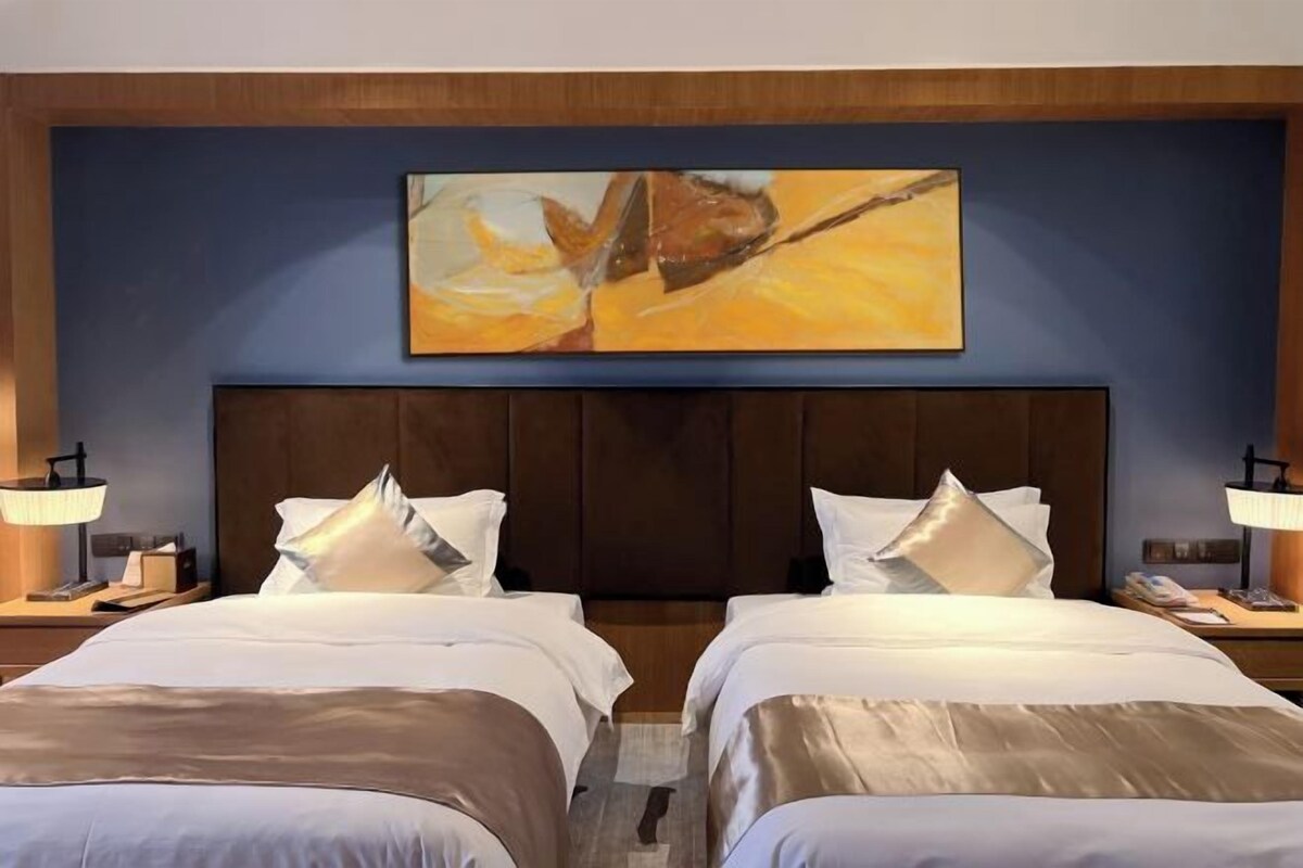 Una habitación de hotel con dos camas, un cuadro grande en la pared y una mesita de noche con una lámpara.