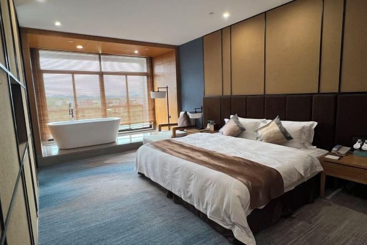 Una habitación de hotel moderna con una cama grande, una bañera y vistas al exterior.