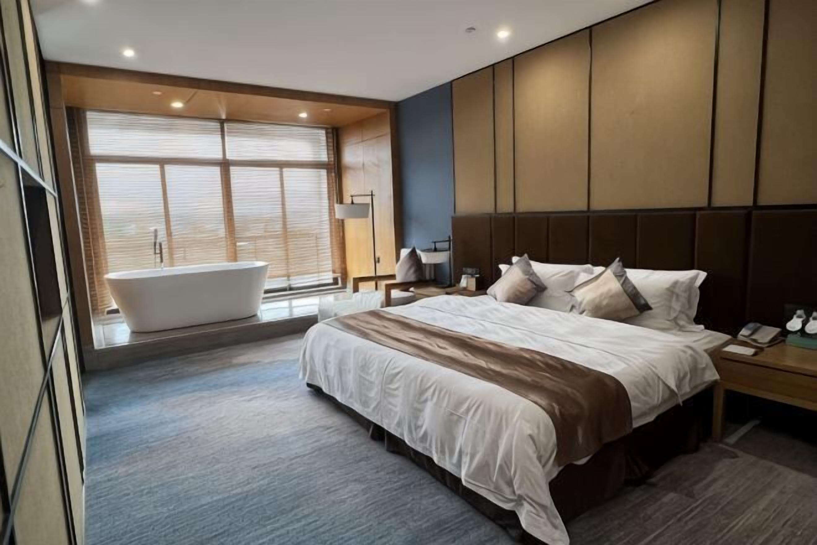 Ein modernes Hotelzimmer mit einem großen Bett, einer Badewanne und einem großen Fenster.
