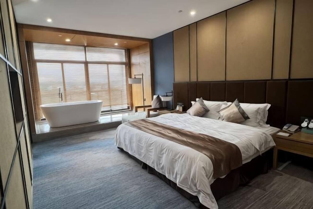 A modern hotel room with a large bed, a bathtub, and a large window.