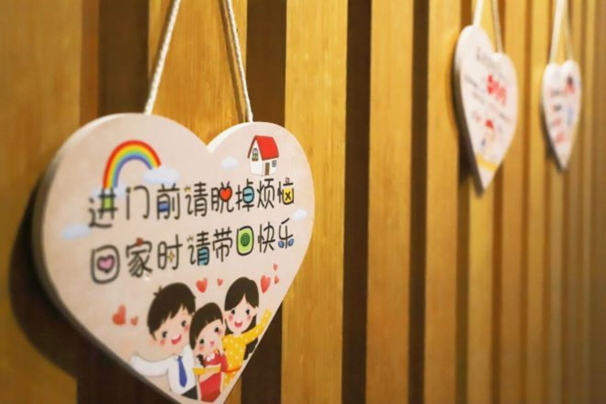 A heart-shaped sign with text and a rainbow, hanging on a wooden wall.