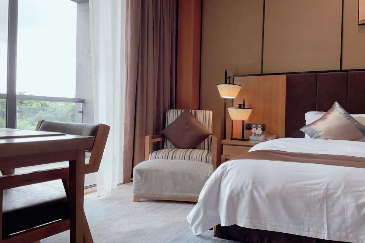 Una habitación de hotel con cama, una silla, un escritorio y una mesita de noche con lámpara.