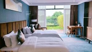 Une chambre d’hôtel avec deux lits, un bureau et une vue sur la verdure environnante.