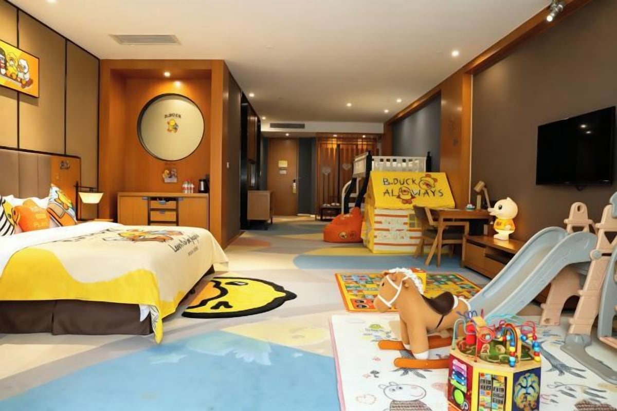 Habitación de hotel con cama, escritorio, silla, televisión y un área de juegos con juguetes.