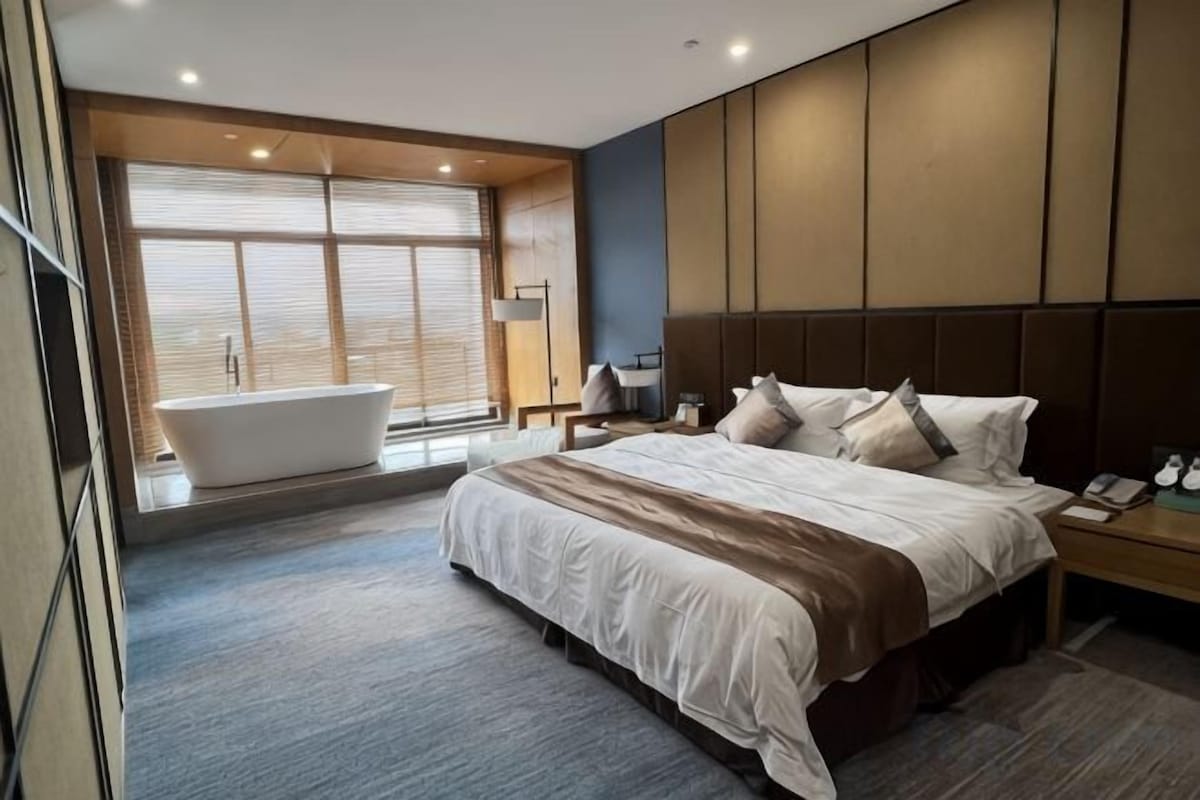Una habitación de hotel moderna con una cama grande, una bañera y un amplio ventanal.